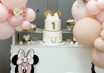 Minnie Mouse first birthday cake with pink and beige balloon arch and character cutout