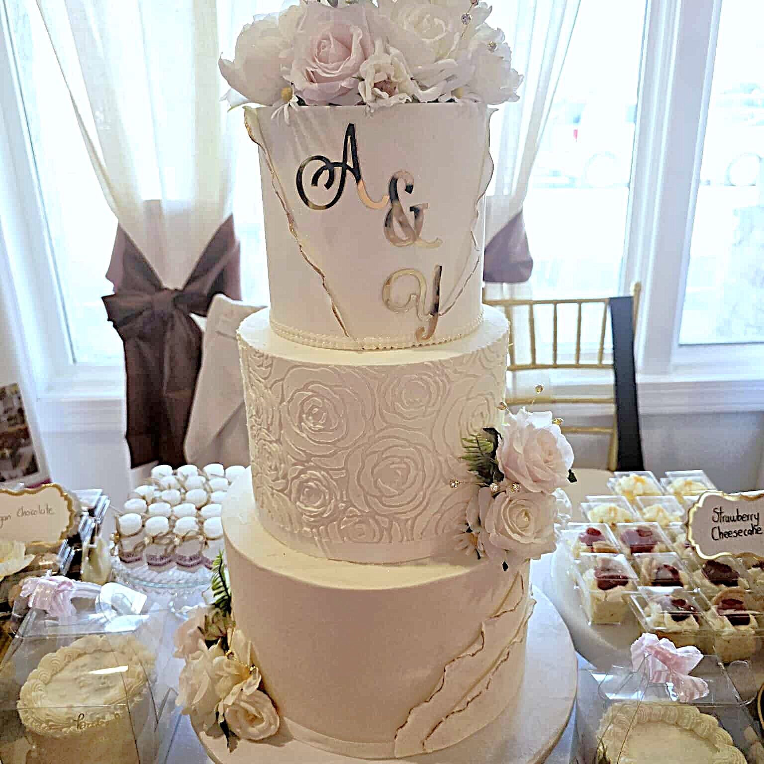Three-tiered wedding cake with floral decor and gold “Mr & Mrs” topper, surrounded by assorted desserts