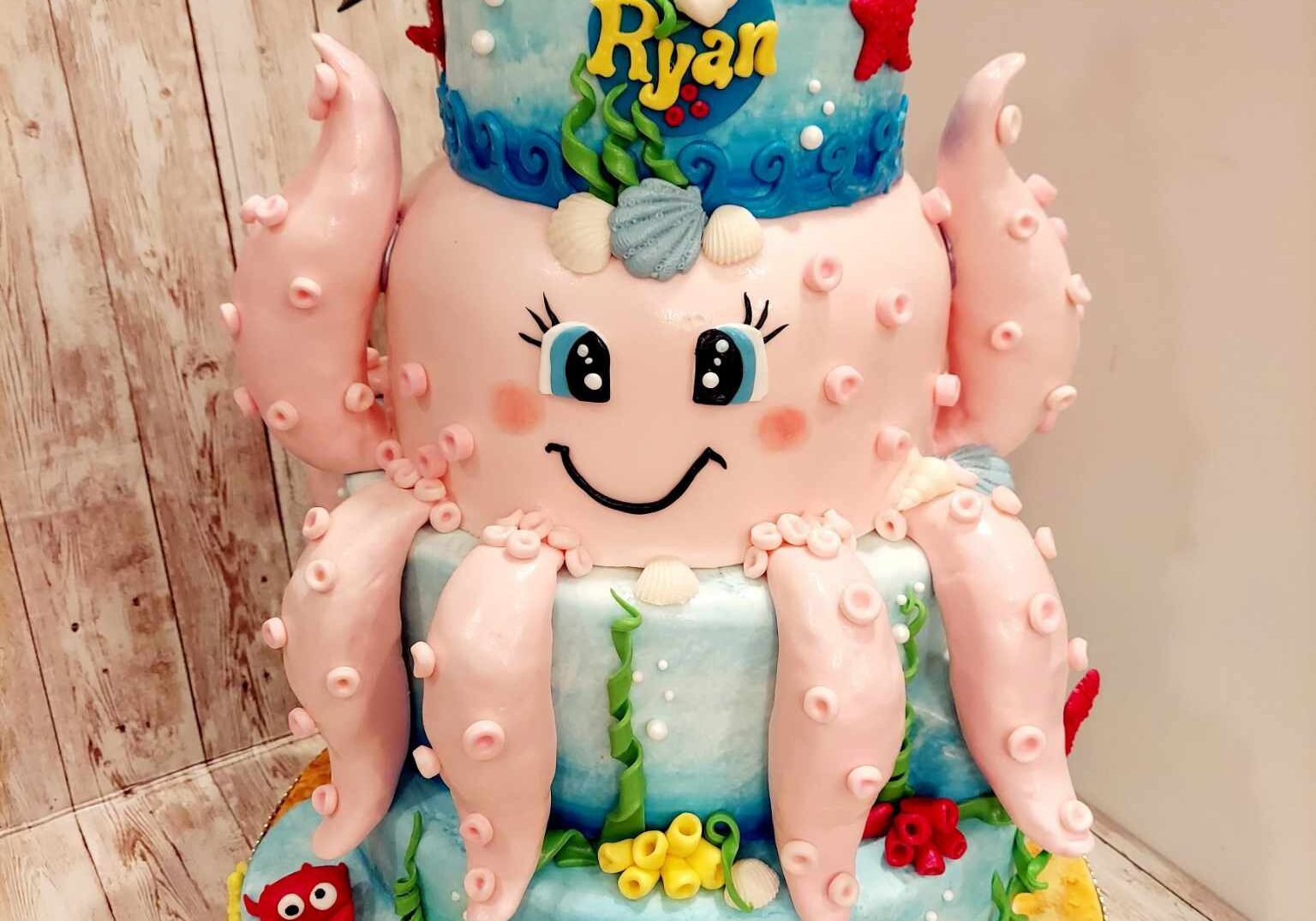 Under-the-sea themed birthday cake with smiling octopus, sea creatures, and “Ryan” name topper