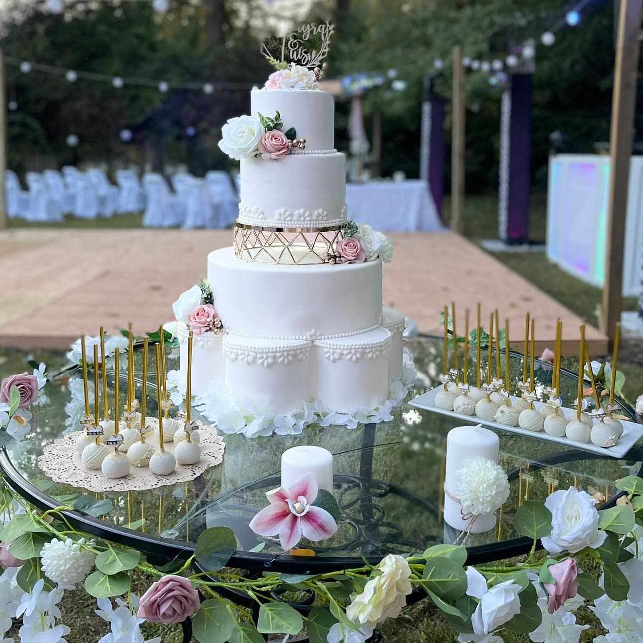 Outdoor white and blush wedding cake setup with floral accents and matching cake pops