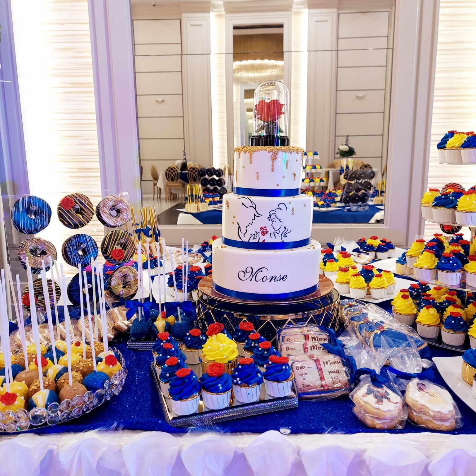 Beauty and the Beast inspired cake with enchanted rose topper, surrounded by blue, yellow, and red themed desserts