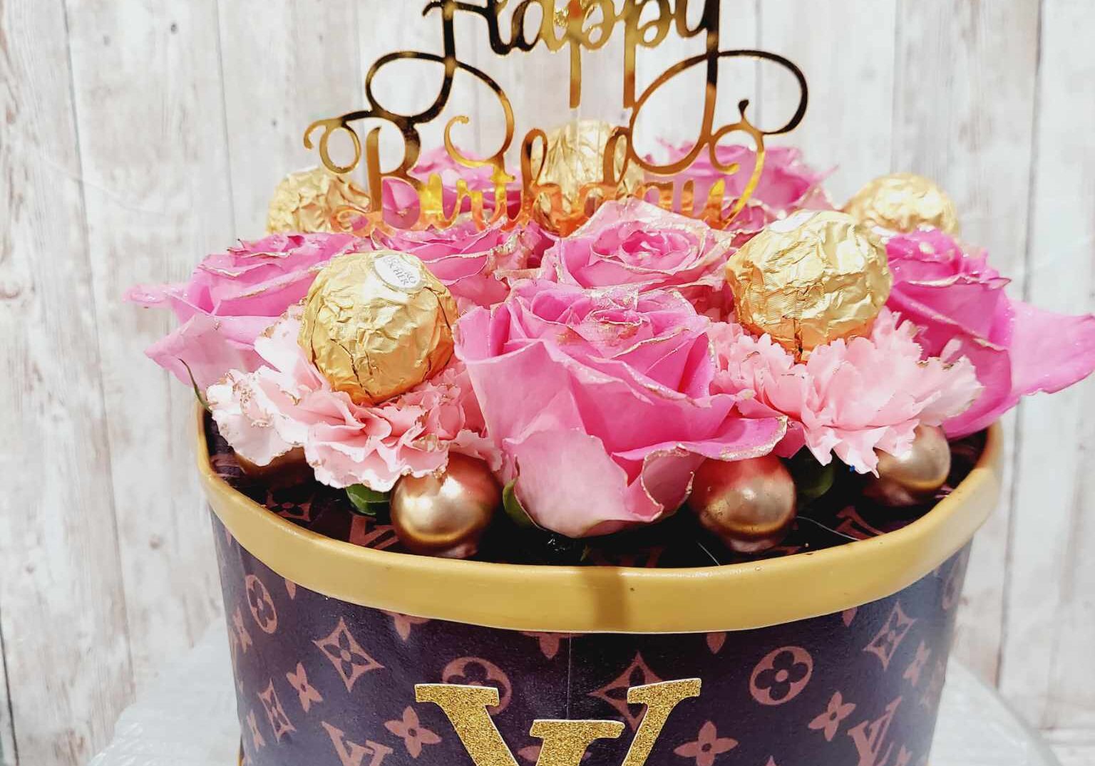 Louis Vuitton themed birthday cake in a hatbox style with pink roses, gold Ferrero Rocher chocolates, and custom topper