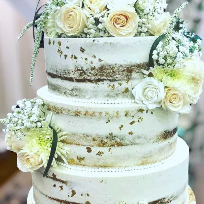 Three-tiered semi-naked wedding cake with white roses, baby’s breath, and gold accents